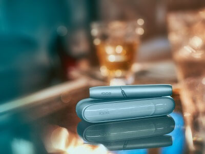 Un support et un chargeur IQOS ORIGINALS DUO turquoise reposant sur une surface en verre.